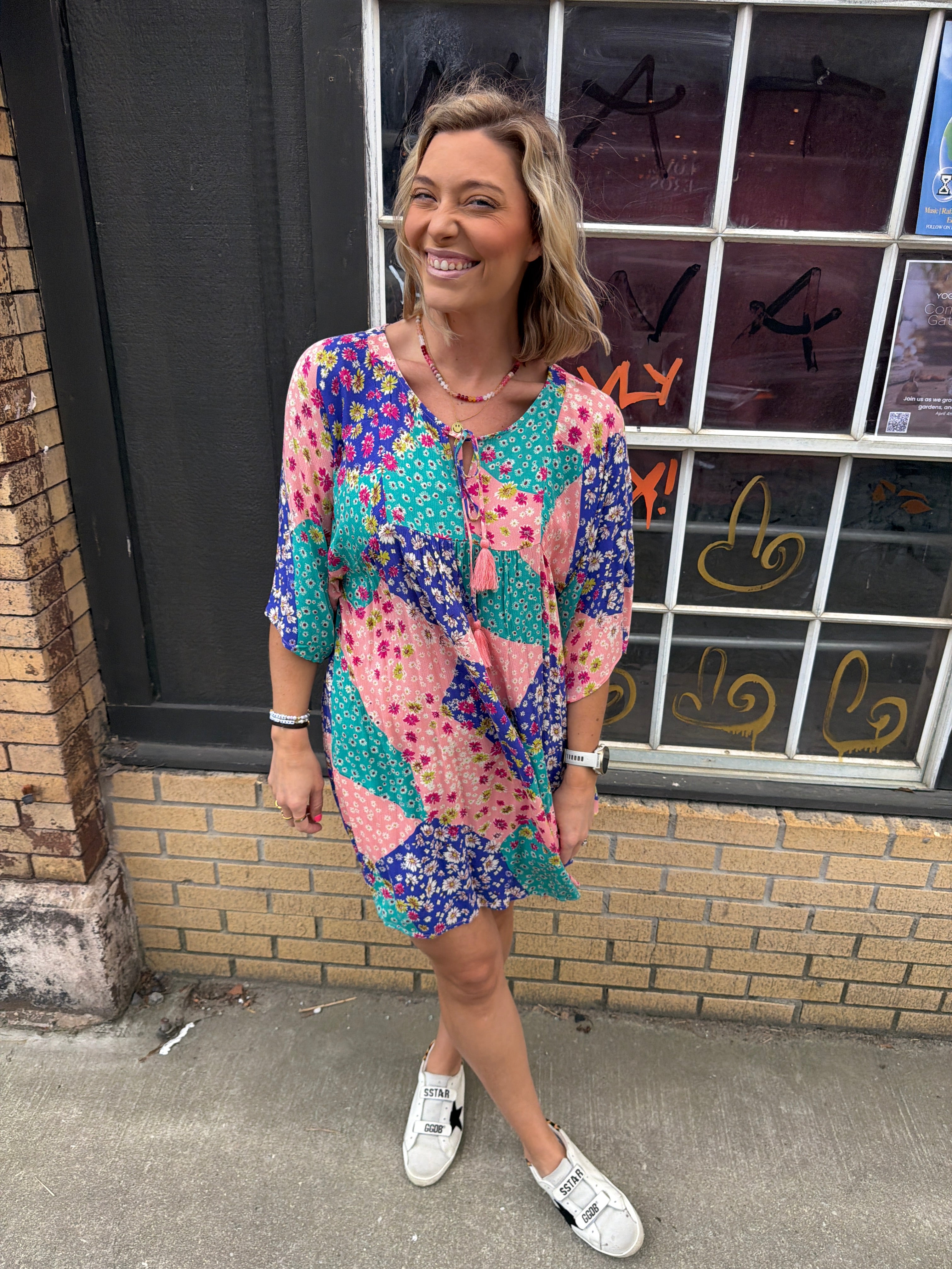woman with a pink blue & teal patterned short dress with elbow length flowy sleeves.