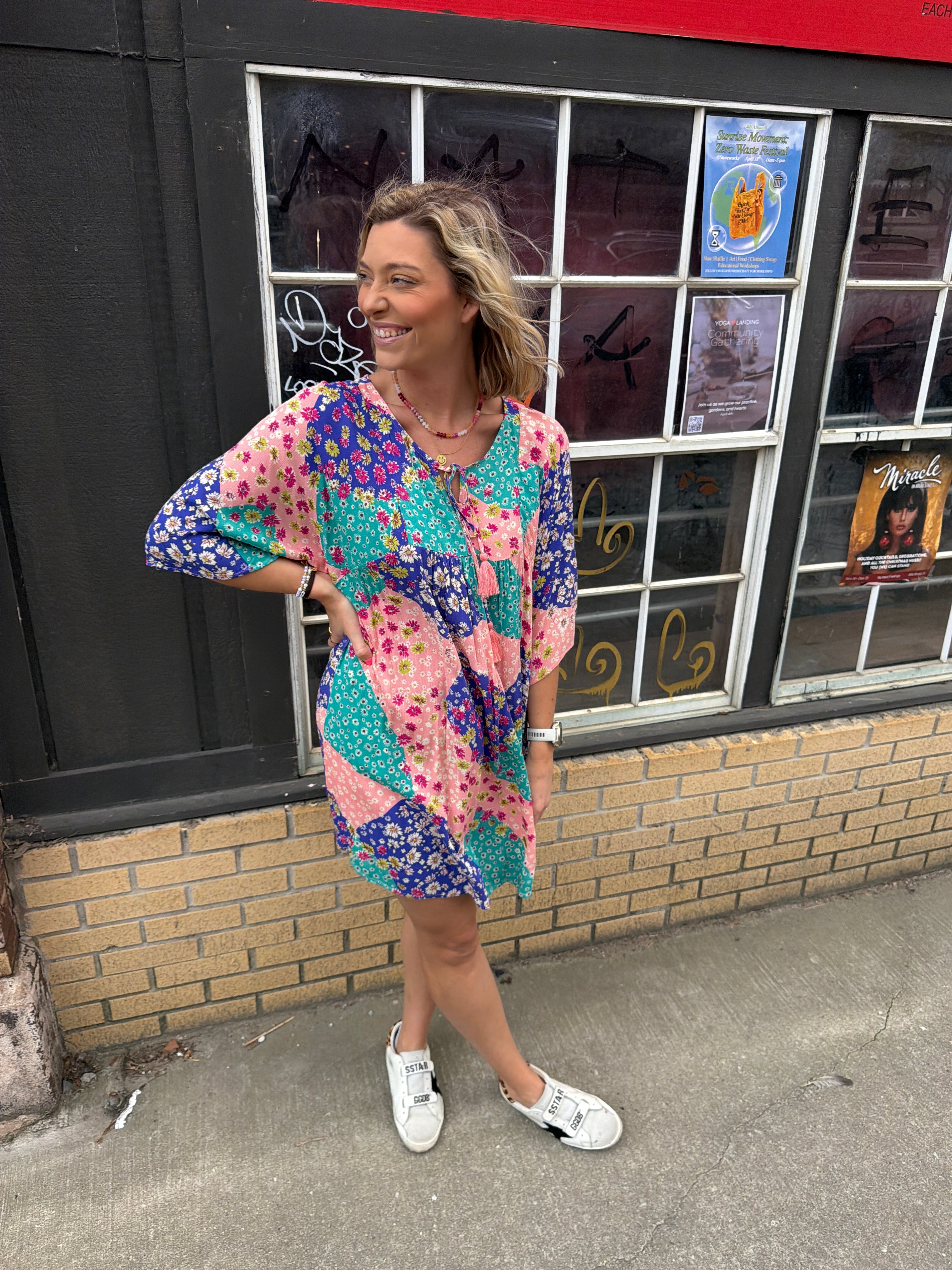 woman with a pink blue & teal patterned short dress with elbow length flowy sleeves.