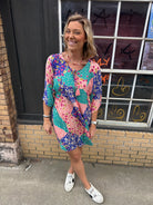 woman with a pink blue & teal patterned short dress with elbow length flowy sleeves.