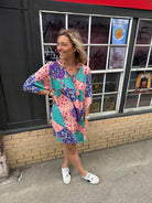 woman with a pink blue & teal patterned short dress with elbow length flowy sleeves.